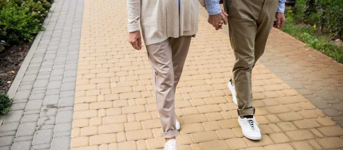 partial view of senior couple walking across paved sidewalk in park